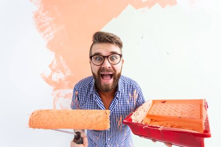 Funny man painting interior wall with paint roller in new house. Guy with roller applying paint on a wall.の写真素材