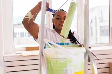 Afro american woman painting an apartment. Renovation, repair and redecoration concept.の写真素材