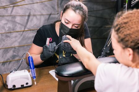 Female master uses an electric machine to remove the nail polish during manicure in the salon. Close-up hardware manicure. Concept of hand care. Female manicurist cleaning of nails by a milling cutter.の写真素材