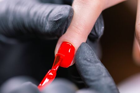 CloseUp shot of master in rubber gloves covering red nails with top coat in the beauty salon. Perfect nails manicure process.の写真素材
