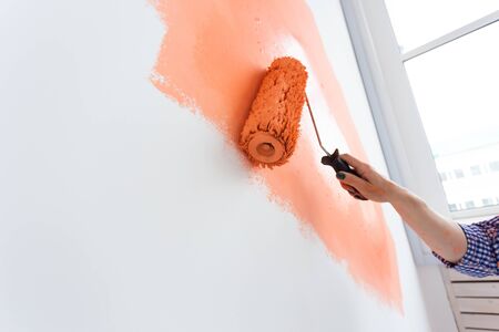 Happy middle-aged woman painting wall in her new apartment. Renovation, redecoration and repair