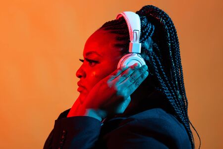 Neon portrait of young african woman listening music with earphones.の写真素材