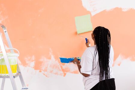 Repair in the apartment. Happy young woman paints the wall with paintの写真素材