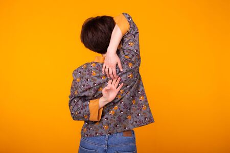 Cute and cheerful woman in home wear pajama studio lifestyle yellow background emotions. Back view.