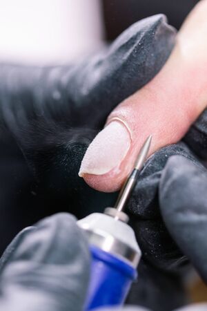 Woman use electric nail file drill in beauty salon. Nails manicure process in detail. Gel polish close-up concept.の写真素材