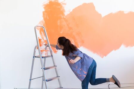Renovation, redecoration and repair concept - Cheerful woman painting wall in new home.