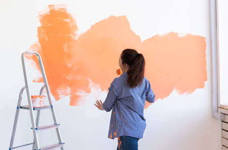 Dancing funny woman painting wall in her new apartment. Renovation and redecoration concept.