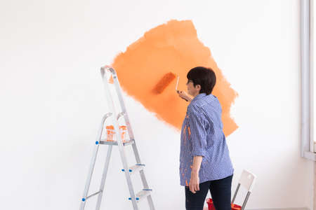 Smiling middle-aged woman painting interior wall of home. Renovation, repair and redecoration concept.の写真素材