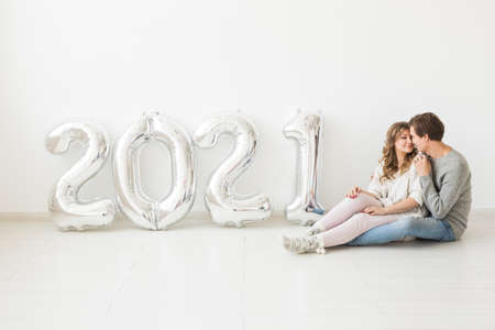 Holidays, festive and party concept - Happy loving couple holds silver 2021 balloons on white background. New Year celebration.の写真素材