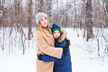 Portrait of happy mother with child son in winter outdoors. Snowy park. Single parent.