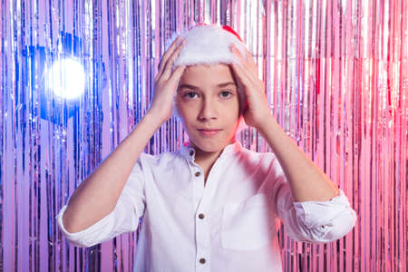 Christmas time. Teen boy with Santa Claus Hat over shiny festive background. Christmas holidays...