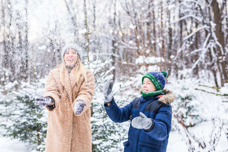 Parenting, fun and season concept - Happy mother and son having fun and playing with snow in winter forestの写真素材