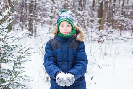 Cute young boy plays with snow, have fun, smiles. Teenager in winter park. Active lifestyle, winter...