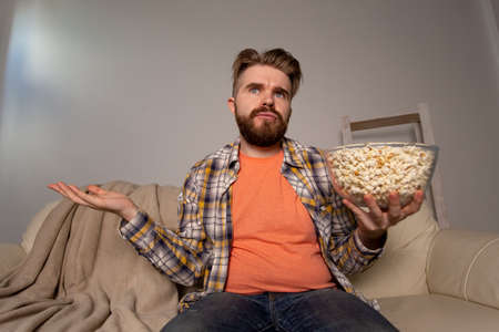 Bearded man watching film or sport games TV eating popcorn in house at night. Cinema, championship and fan concept.の写真素材