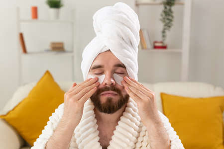 Bearded man applying eye patches on his face. Wrinkles and face home care for men.の写真素材