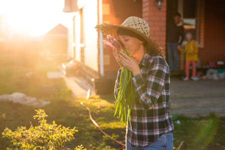 Joyful woman gardener sniffs bunch of green onions on sunny warm spring day. Plant care and harvest concept and hobbyの写真素材