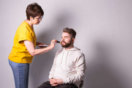 Bearded man getting makeup. Woman visagist works with brush. Copyspace