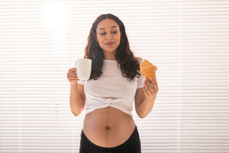Happy pregnant woman with croissant buns at home. Pregnancy, eating and people conceptの写真素材
