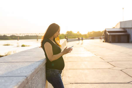 Pregnant woman with smartphone outdoors. Pregnancy, technology and communication concept