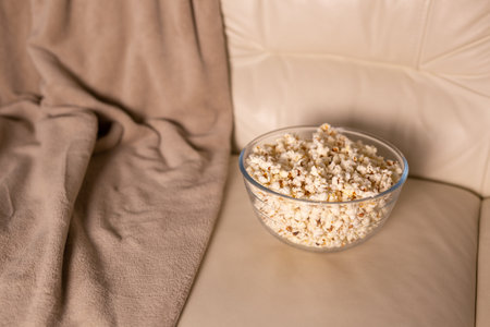 Bowl of popcorn for watching a film on a beige couch. Snacks and unhealthy junk food conceptの写真素材