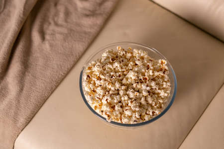 Bowl of popcorn for watching a film on a beige couch. Snacks and unhealthy junk food conceptの写真素材