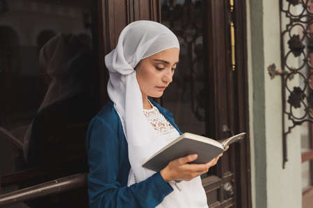 Portrait of young muslim woman wearing hijab reading book outdoorsの写真素材