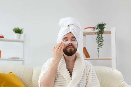 Bearded man applying eye patches on his face. Wrinkles and face home care for men.の写真素材