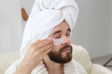 Bearded man applying eye patches on his face. Wrinkles and face home care for men.