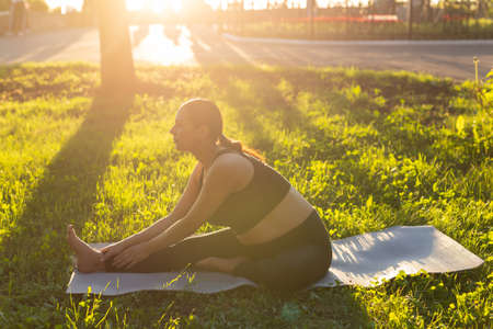 Peaceful young positive pregnant woman in gymnastic suit does yoga and meditate sitting on mat on...