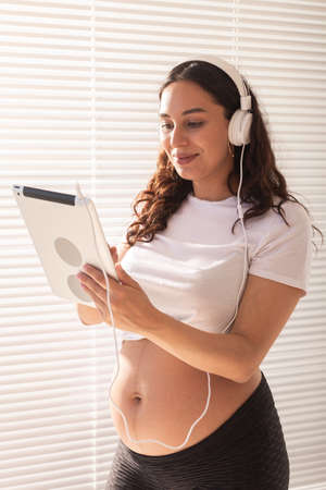 Pregnant woman listening music in headphones with digital tabletの写真素材