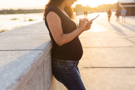 Close-up of pregnant woman with smartphone at park. Pregnancy, technology and communication concept.