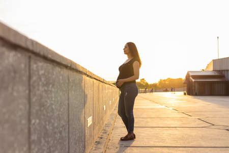 Portrait of hispanic pregnant woman walking on embankment at sunset. Pregnancy and motherhood concept. Advertising area workspaceの写真素材
