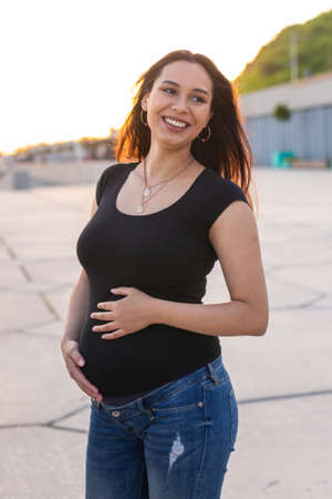Portrait of hispanic pregnant woman walking on embankment at sunset. Pregnancy and motherhood...
