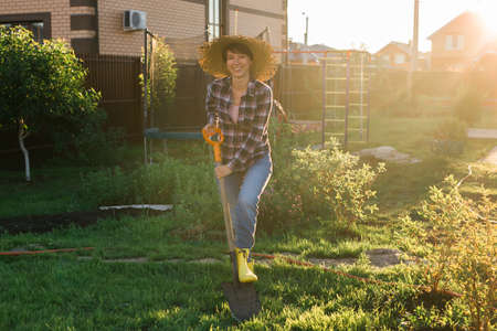 Positive female gardener digs the beds with shovel on sunny warm spring day. Plant care and planting concept for the new seasonの写真素材