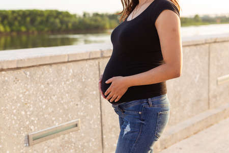 Close-up of pregnant belly outdoors copyspace. Pregnancy and motherhood concept.