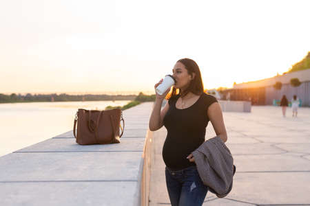 Hispanic pregnant woman drinking take away coffee outdoors. Copy space.の写真素材
