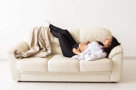 Hispanic pregnant woman lying on sofa at home. Pregnancy, resting and expectation concept.の写真素材