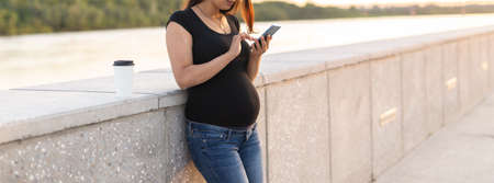 Pregnant woman with smartphone at park. Pregnancy, technology and communication concept. Copy space.の写真素材