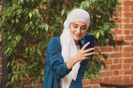 Muslim woman taking selfie. Happy beautiful girl with scarf take picture of her self using smartphone.の写真素材
