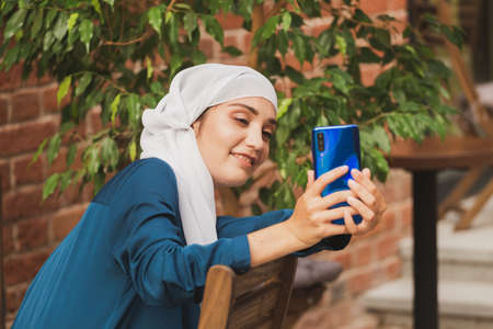 Muslim woman taking selfie. Happy beautiful girl with scarf take picture of her self using smartphone.の写真素材