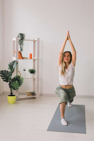 Woman practise yoga performs. Pose on mat inside of cozy room with plants and greenery. Healthy lifestyle concept.の写真素材
