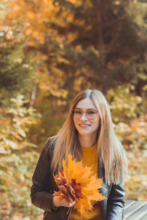 Cute smiley woman holding autumn leaves in fall park. Seasonal, lifestyle and leisure concept.の写真素材