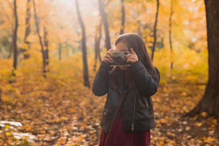 Child girl using an old-fashioned camera in autumn nature. Photographer, fall season and leisure concept.の写真素材
