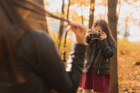 Child girl photographer takes pictures of a mother in the park in autumn. Hobbies, photo art and leisure concept.の写真素材