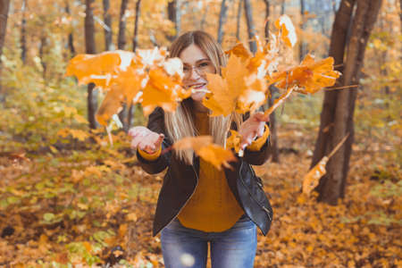 Happy laughing young woman throwing leaves in autumn park. Fall season