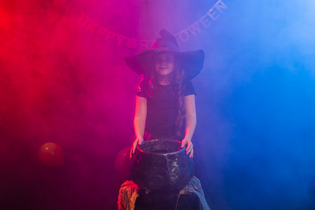 Child girl witch preparing a potion in the cauldron at halloween holidays.