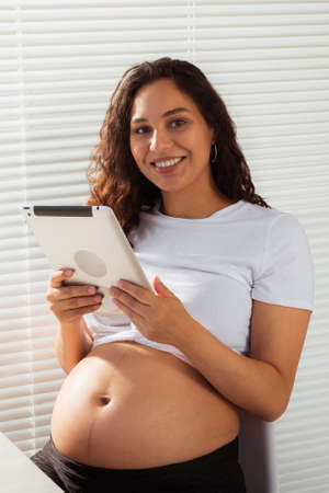Hispanic pregnant woman using digital tablet while breakfast. Technology, pregnancy and maternity leaveの写真素材