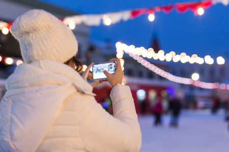 Happy young woman in winter on the ice rink taking picture on smartphone.の写真素材