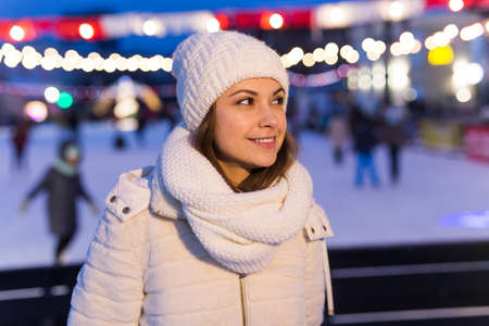 Christmas, winter and leisure concept - happy young woman near ice skating rink outdoors.の写真素材