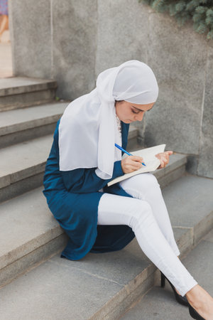 Female middle eastern college student sits on stairs in university campus. Education and knowledge concept.の写真素材